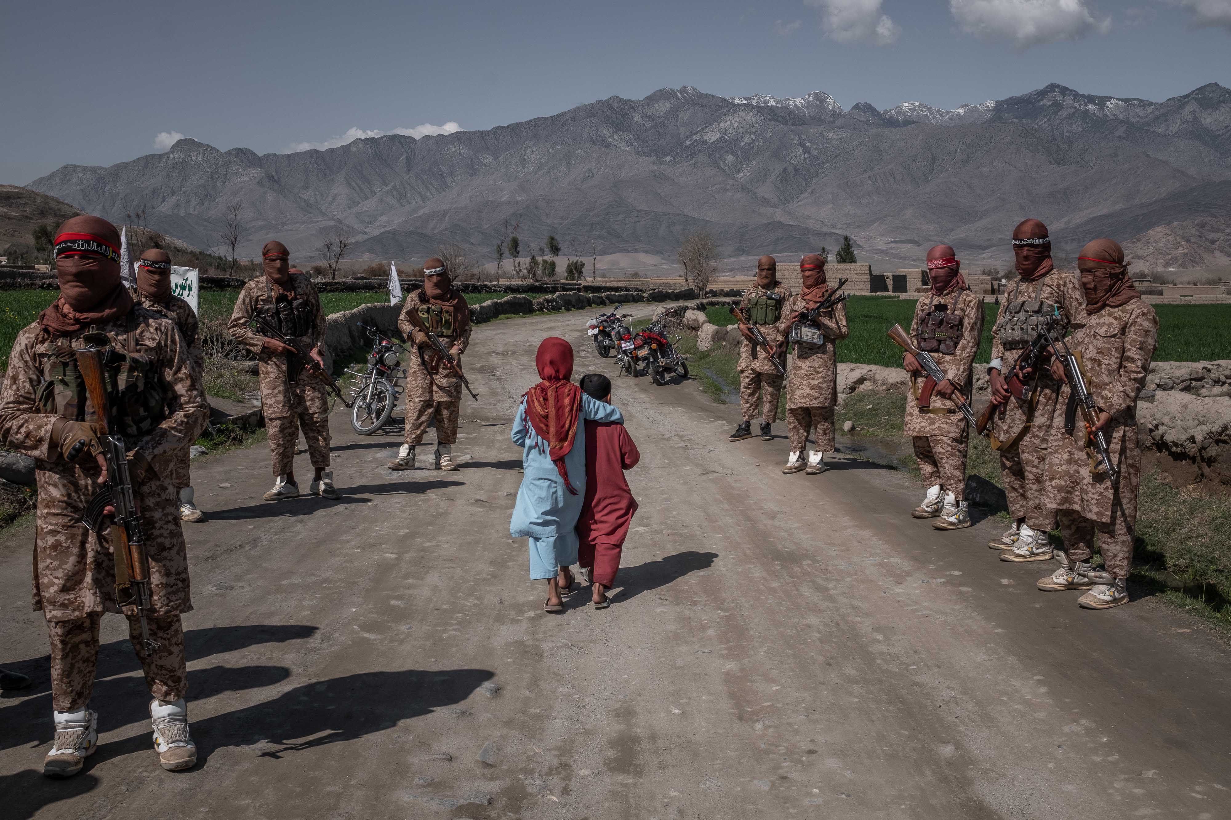 Deux enfants afghans marchent sur une route gardée par des membres de l’Unité rouge des talibans, dans la province de Laghman, à l’est de Kabul, le 13 mars 2020. 