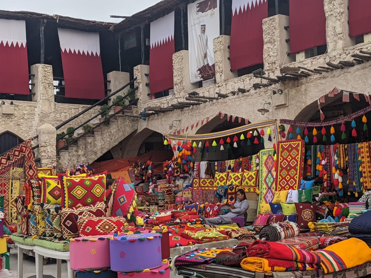 A woman sits in a market stall surrounded by colorful textiles