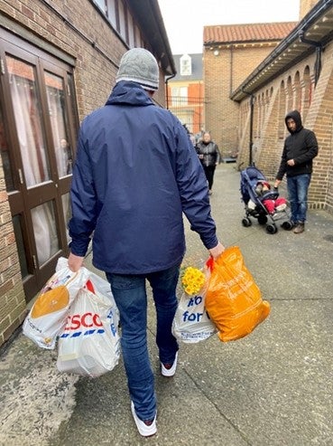 A man in a coat walks down a street carrying grocery bags