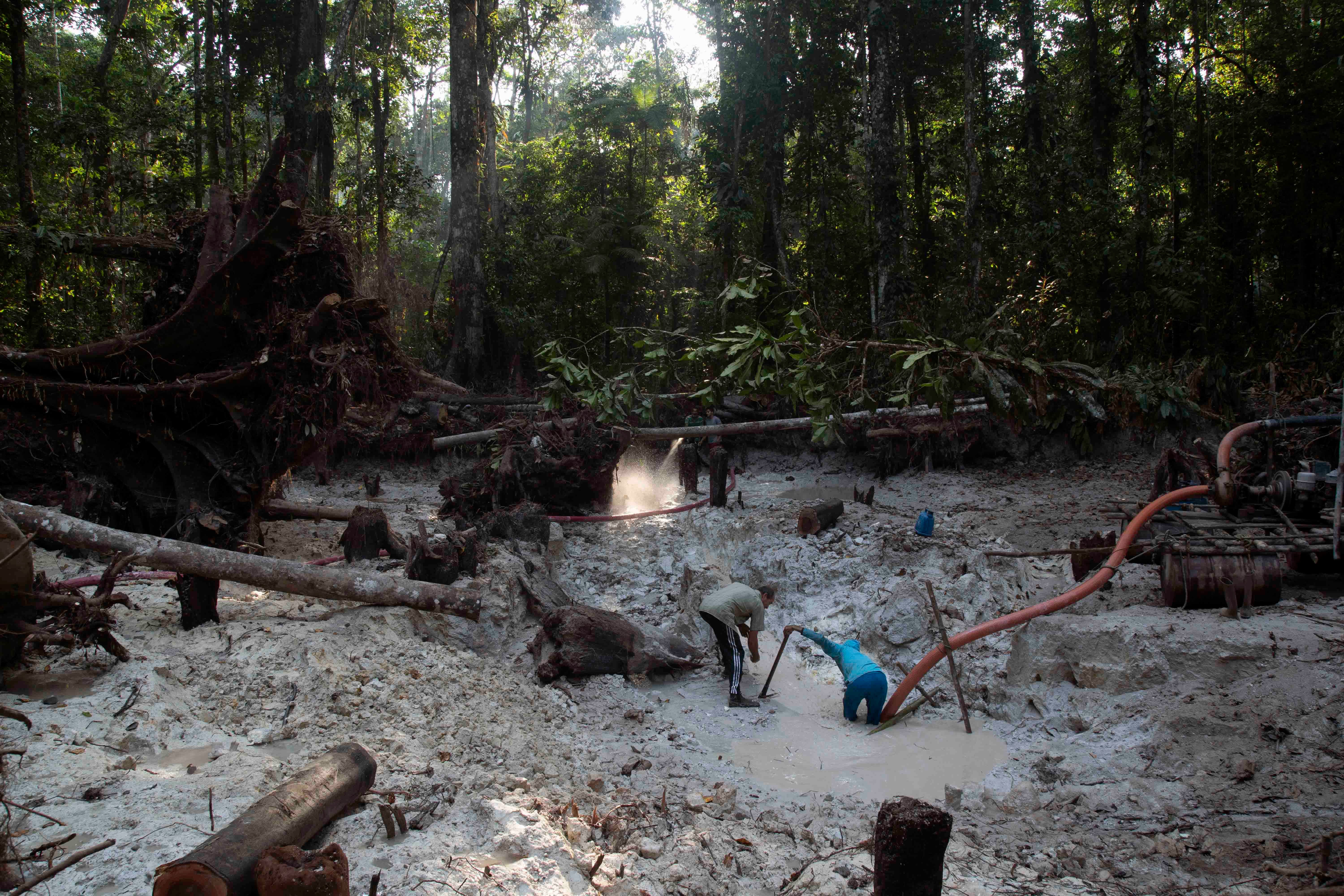 Two people kneel in a mine in a jungle