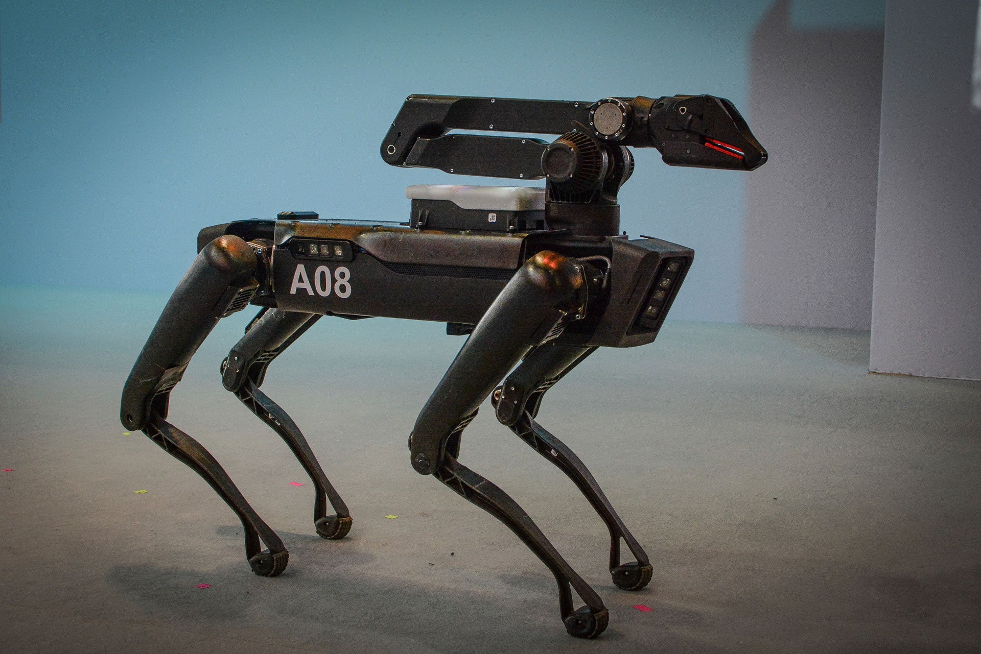 A black robot with four legs resembling a dog stands on a stage in front of a shite background.