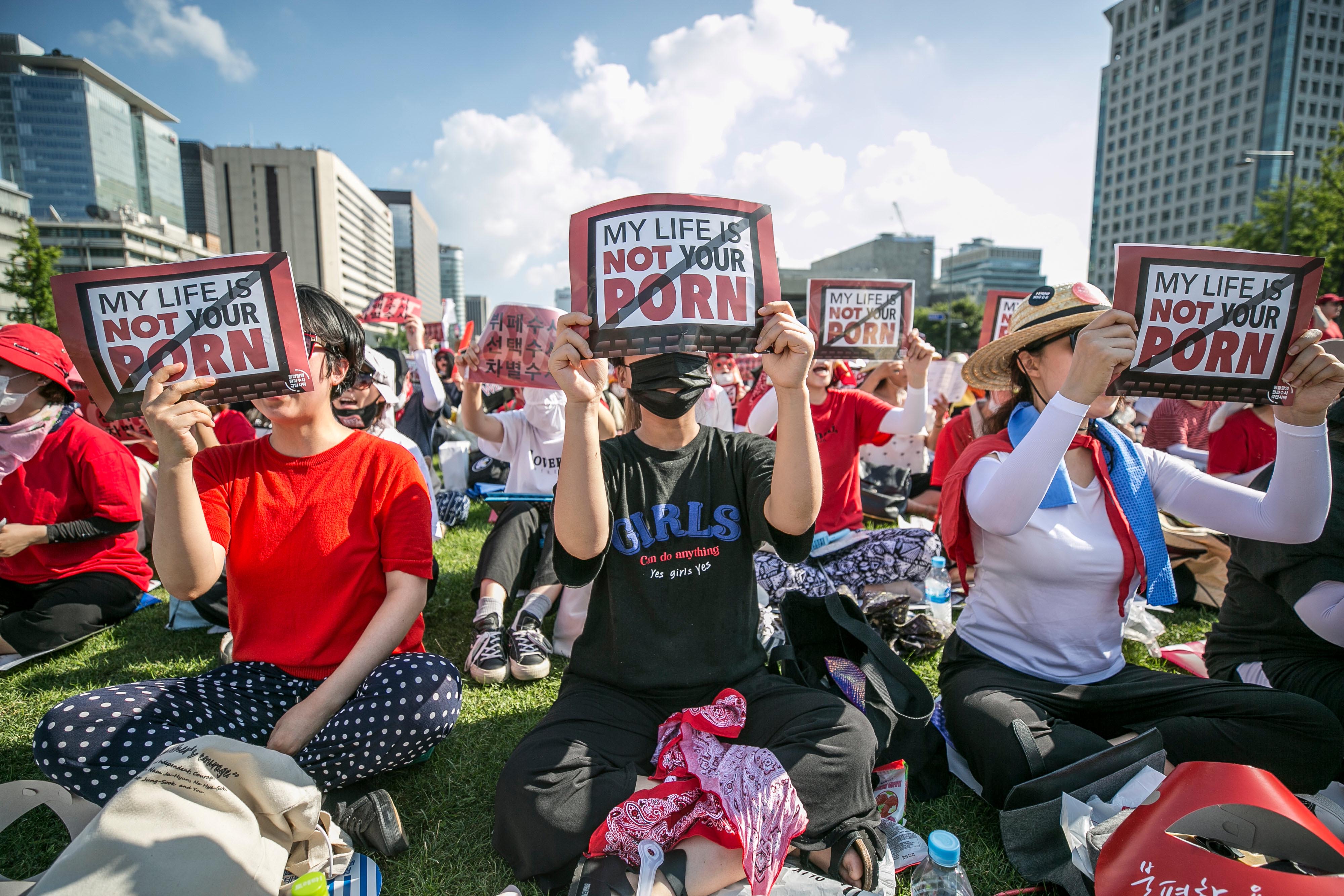 A group of women sit holding protest signs that read "My Life Is Not Your Porn"