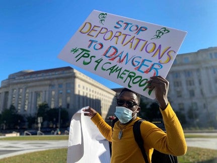 A person holding a protest sign that reads "Stop Deportations to Danger"