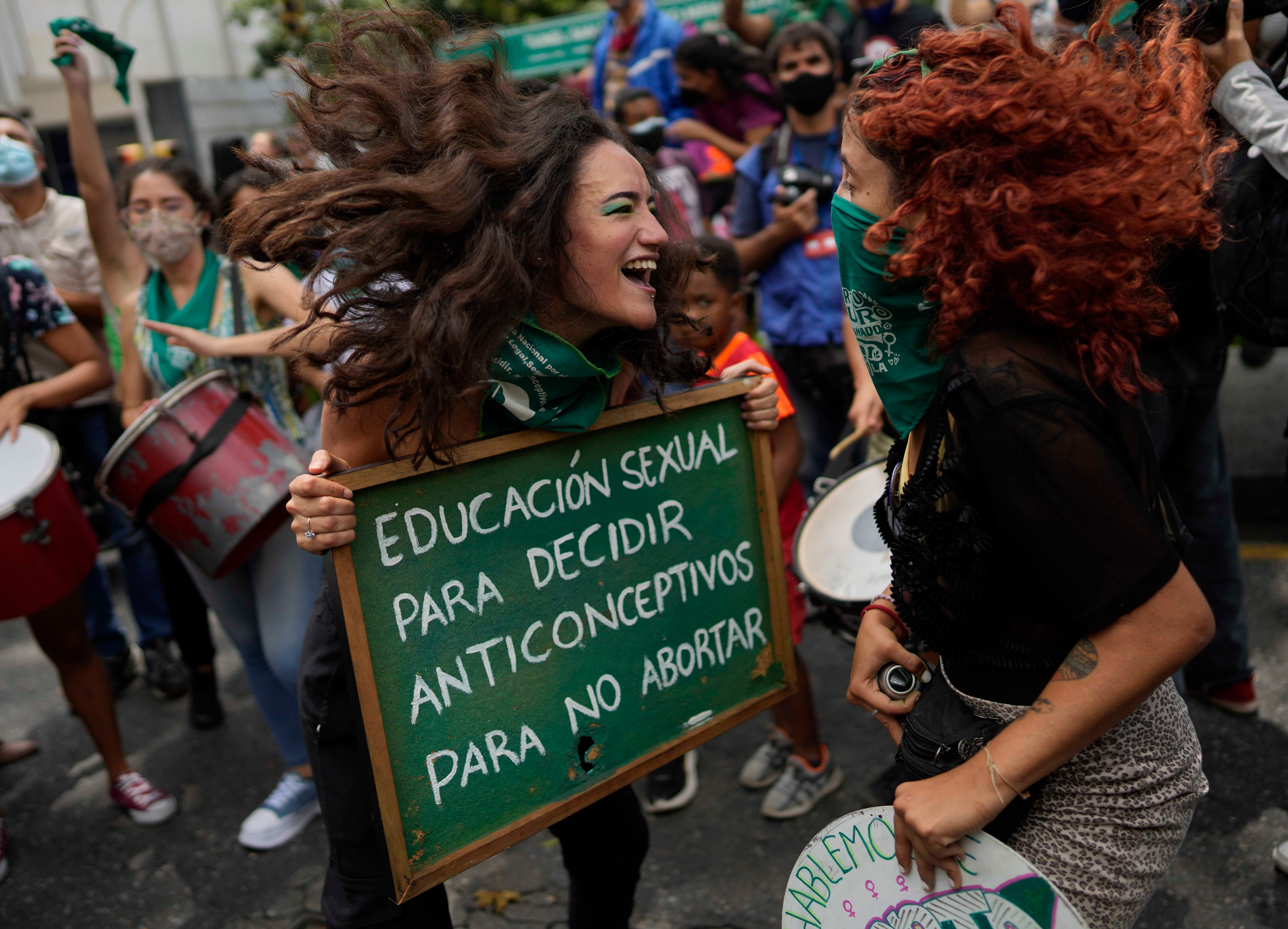 Two women jump and smile while holding a protest sign