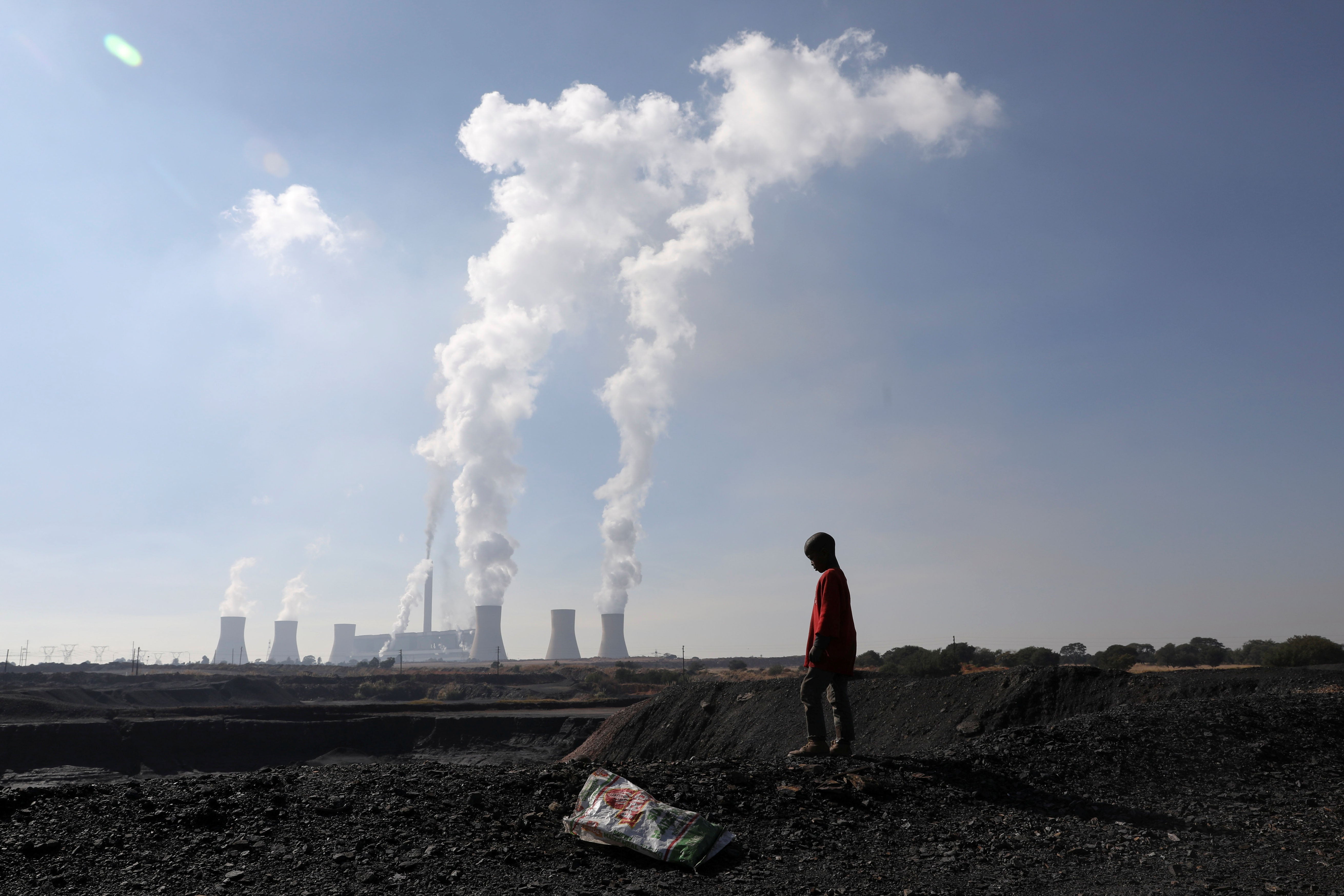 A child collects coal in front of a coal-fired power plant