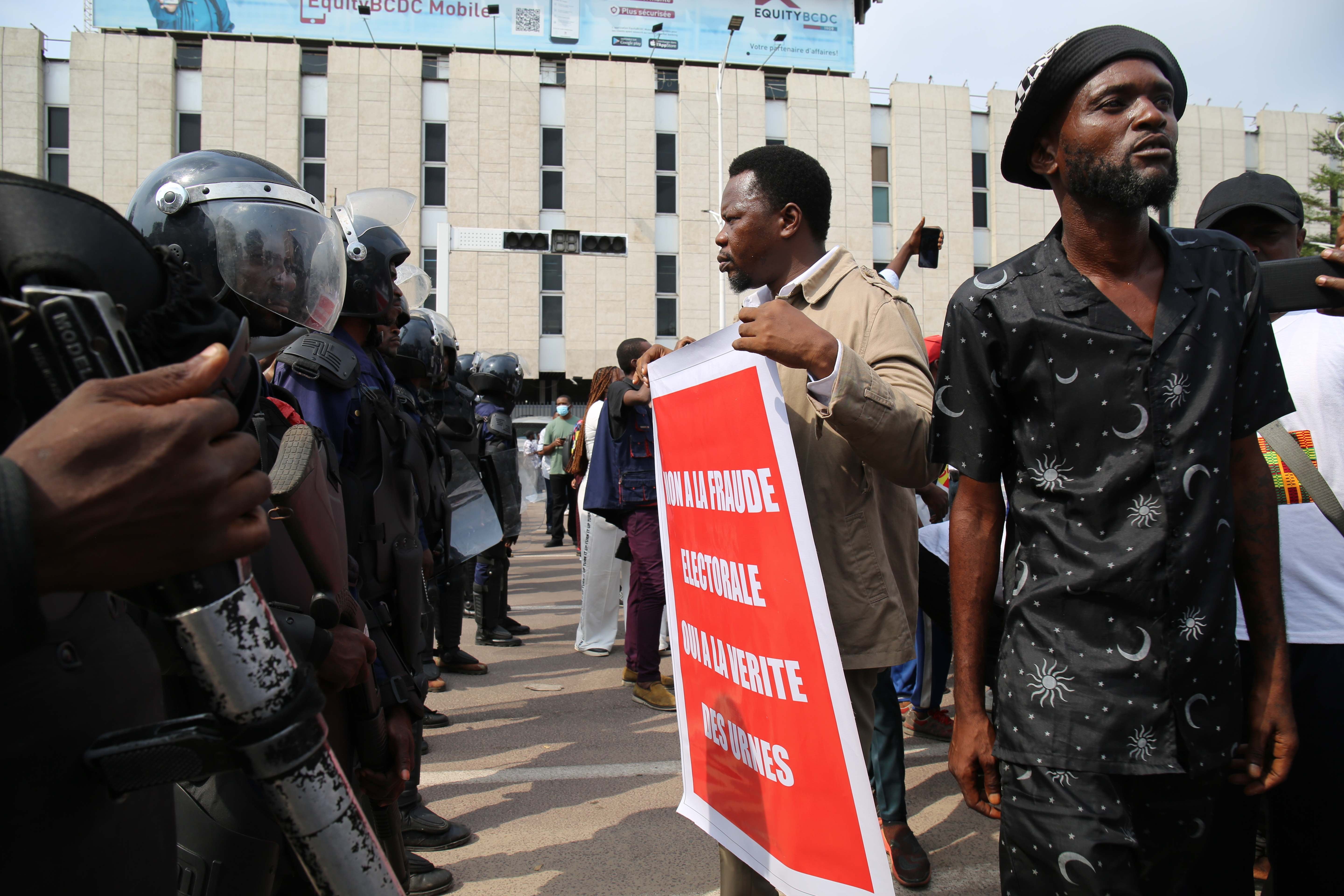 Protester holds sign in front of a line of riot police