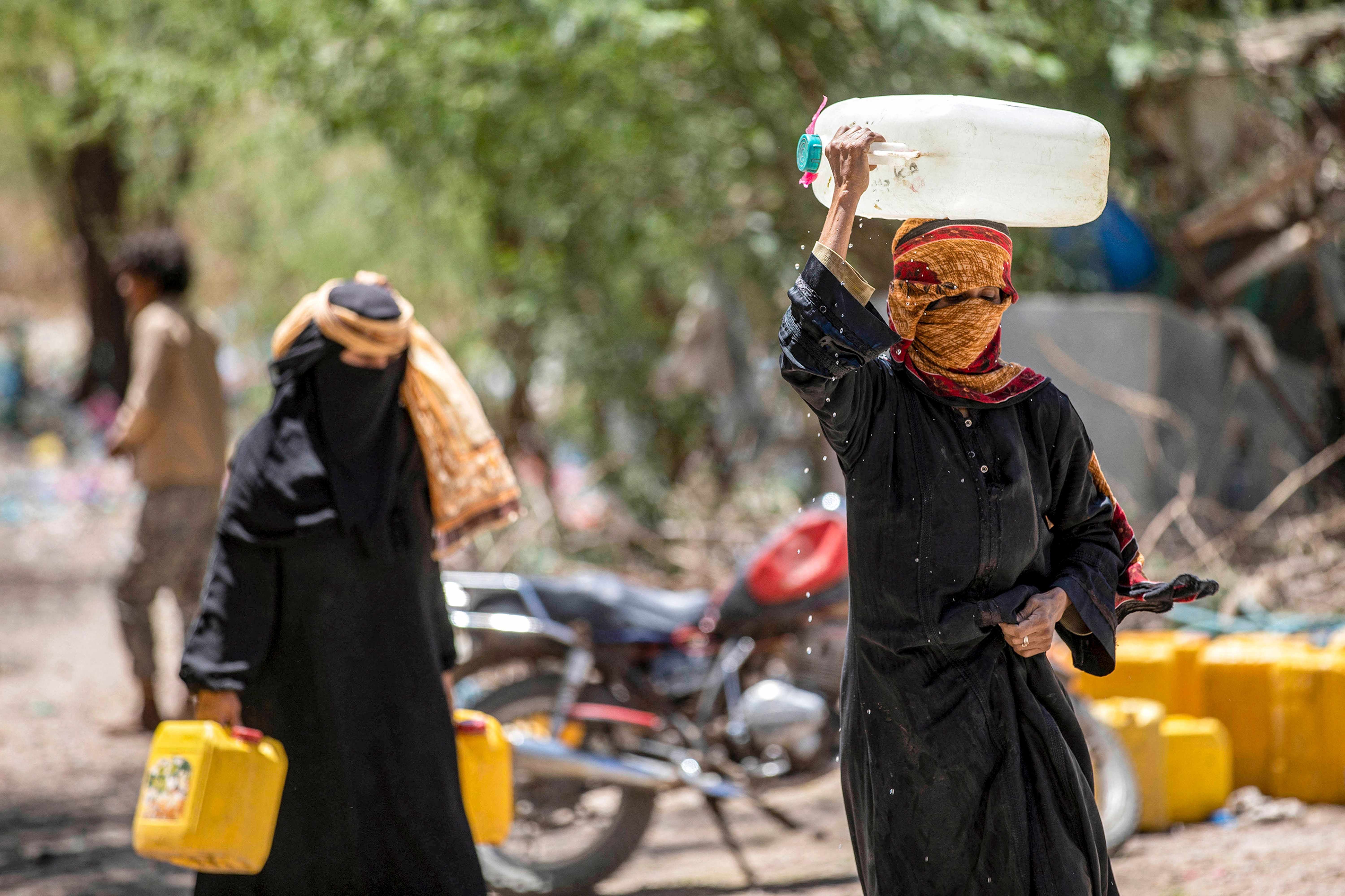 Women walk with canisters filled with water from a tanker truck on the outskirts of Taizz.