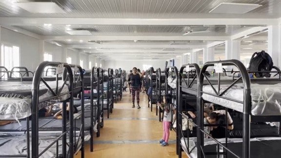 Migrants and asylum seekers walk and rest inside one of the modular containers that serve as dormitories with bunk beds