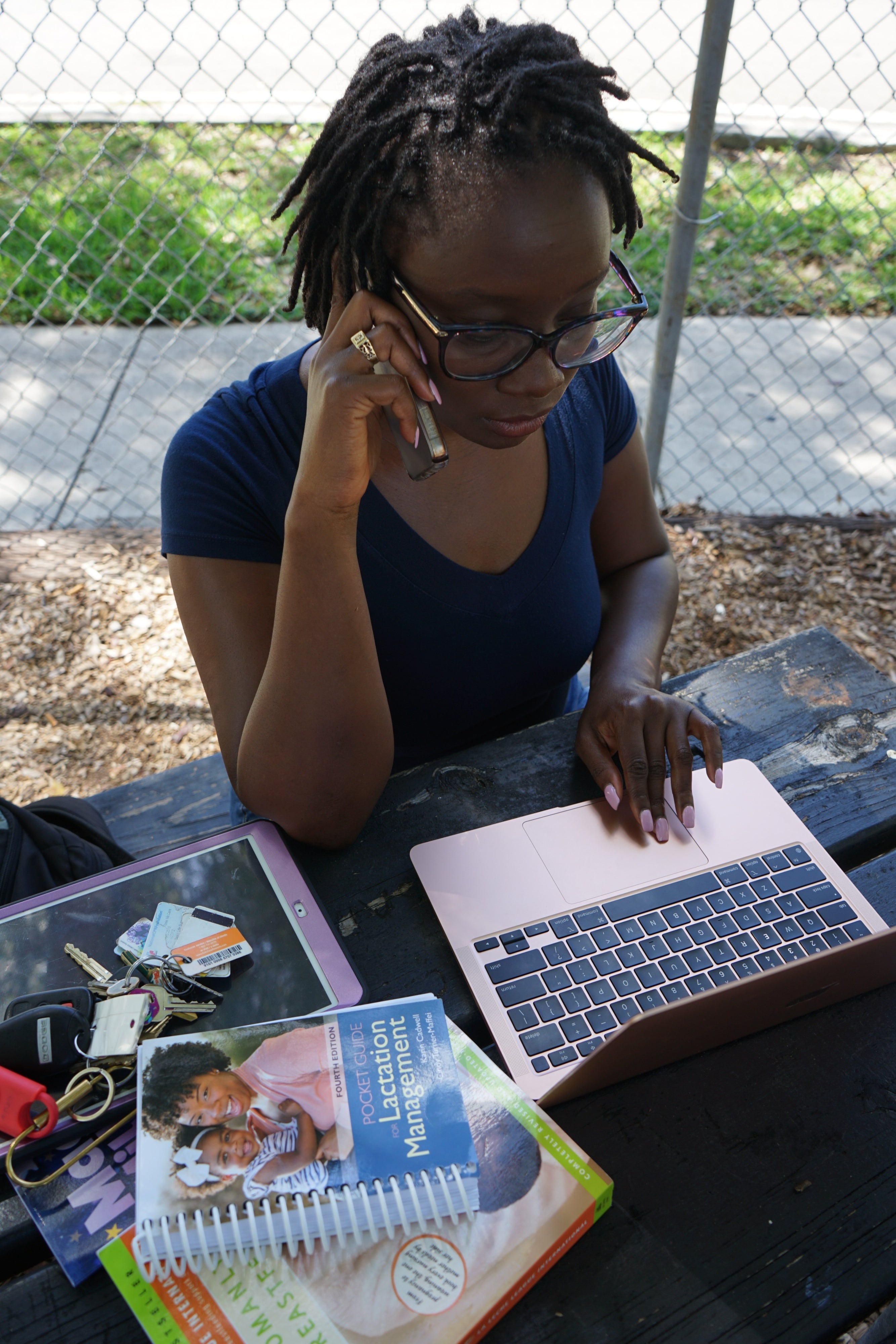 A woman sits at her laptop while on her cell phone