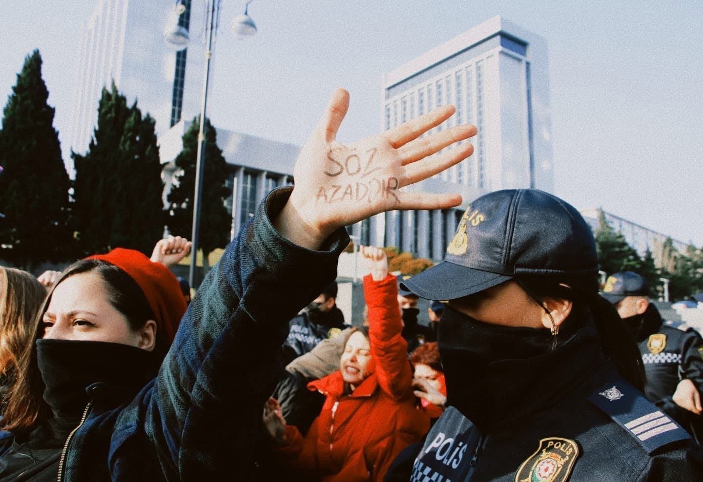 A woman wearing a face mask holds her hand up at a protest