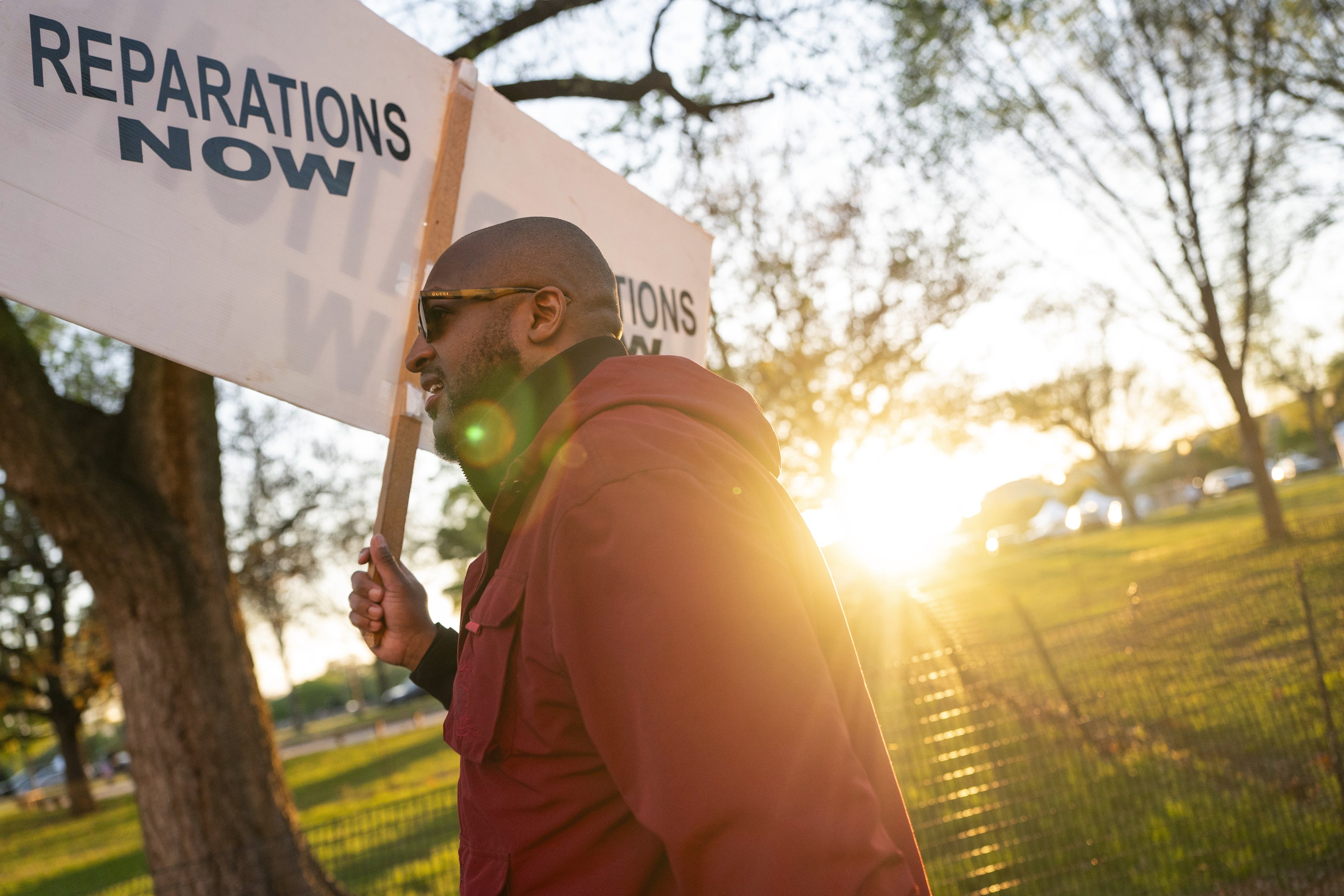 A man holding a sign that reads "Reparations Now"