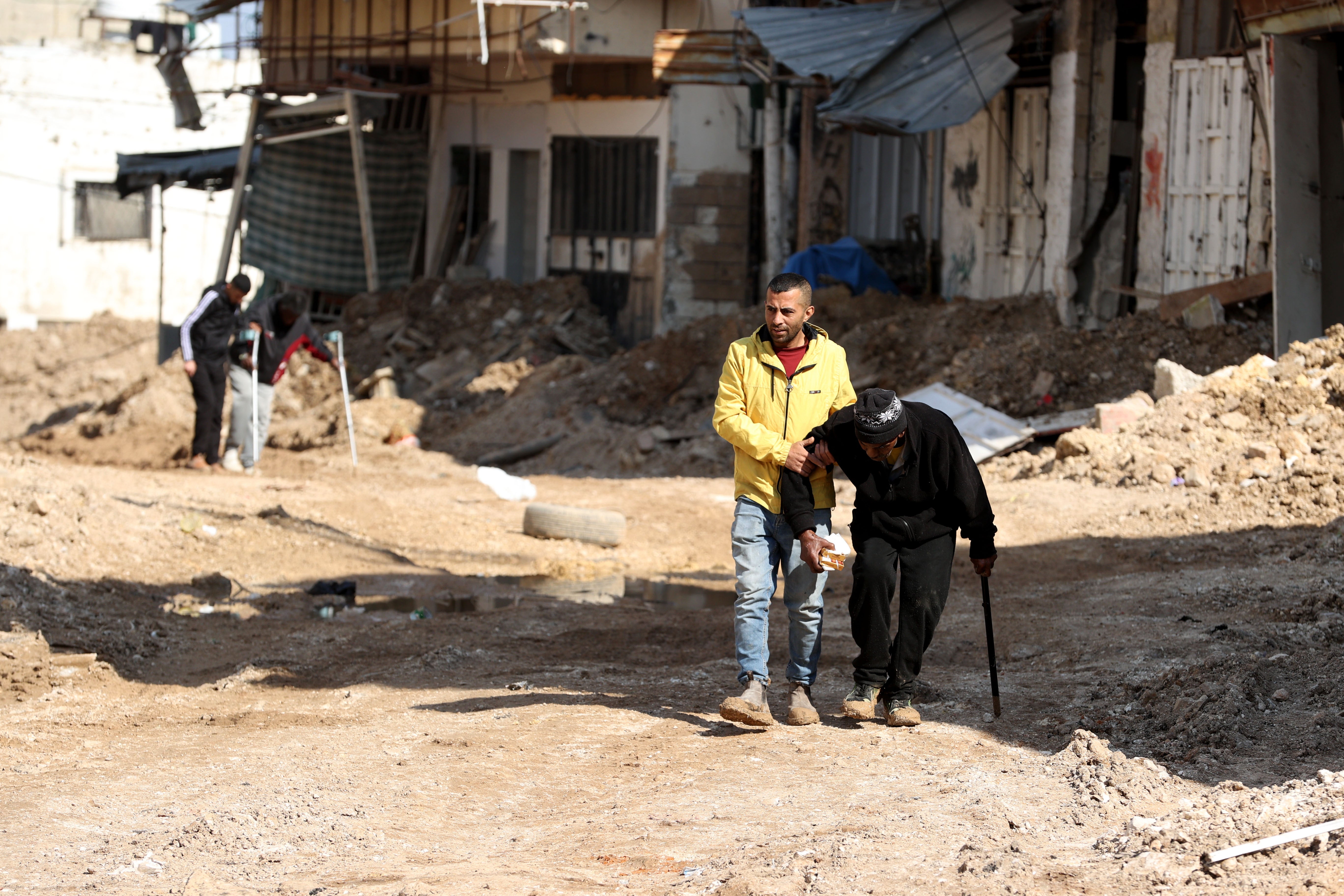 Two people with disabilities, including an older man, are assisted by two other men during the forced displacement by Israeli forces from Tulkarem refugee camp in the northern West Bank