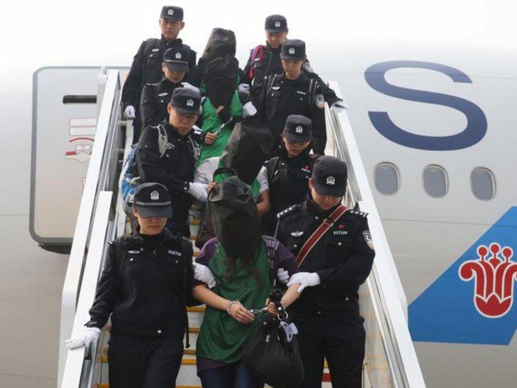 Police escort a group of people deported from Kenya as they get off a plane at Beijing Capital International Airport on April 13, 2016.