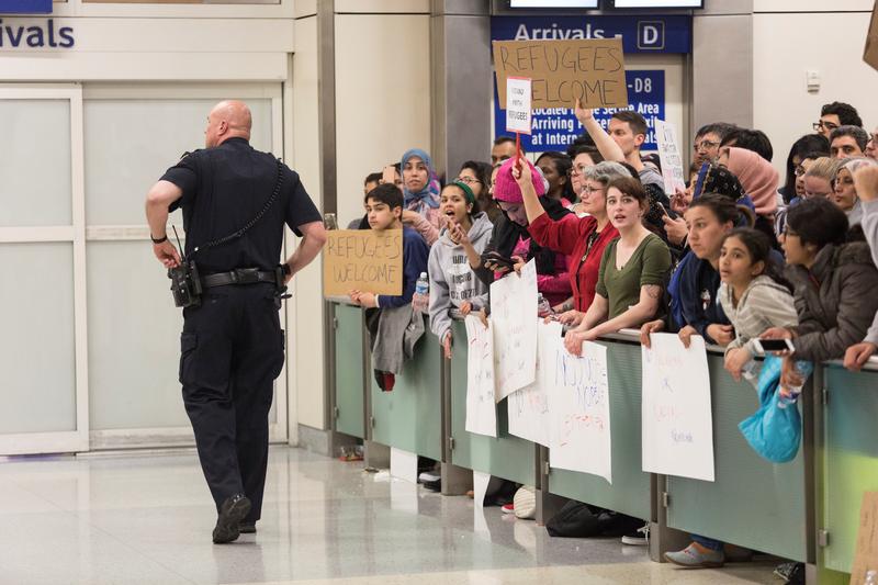 A police officer walks past people as they gather to protest against the travel ban imposed by U.S. President Donald Trump's executive order, at Dallas/Fort Worth International Airport in Dallas, Texas, U.S. January 28, 2017.