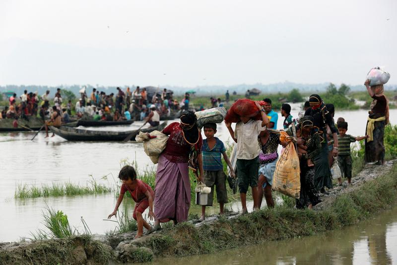 Rohingya refugees walk on a muddy path as others travel on a boat after crossing the Bangladesh-Myanmar border, in Teknaf, Bangladesh, September 6, 2017.