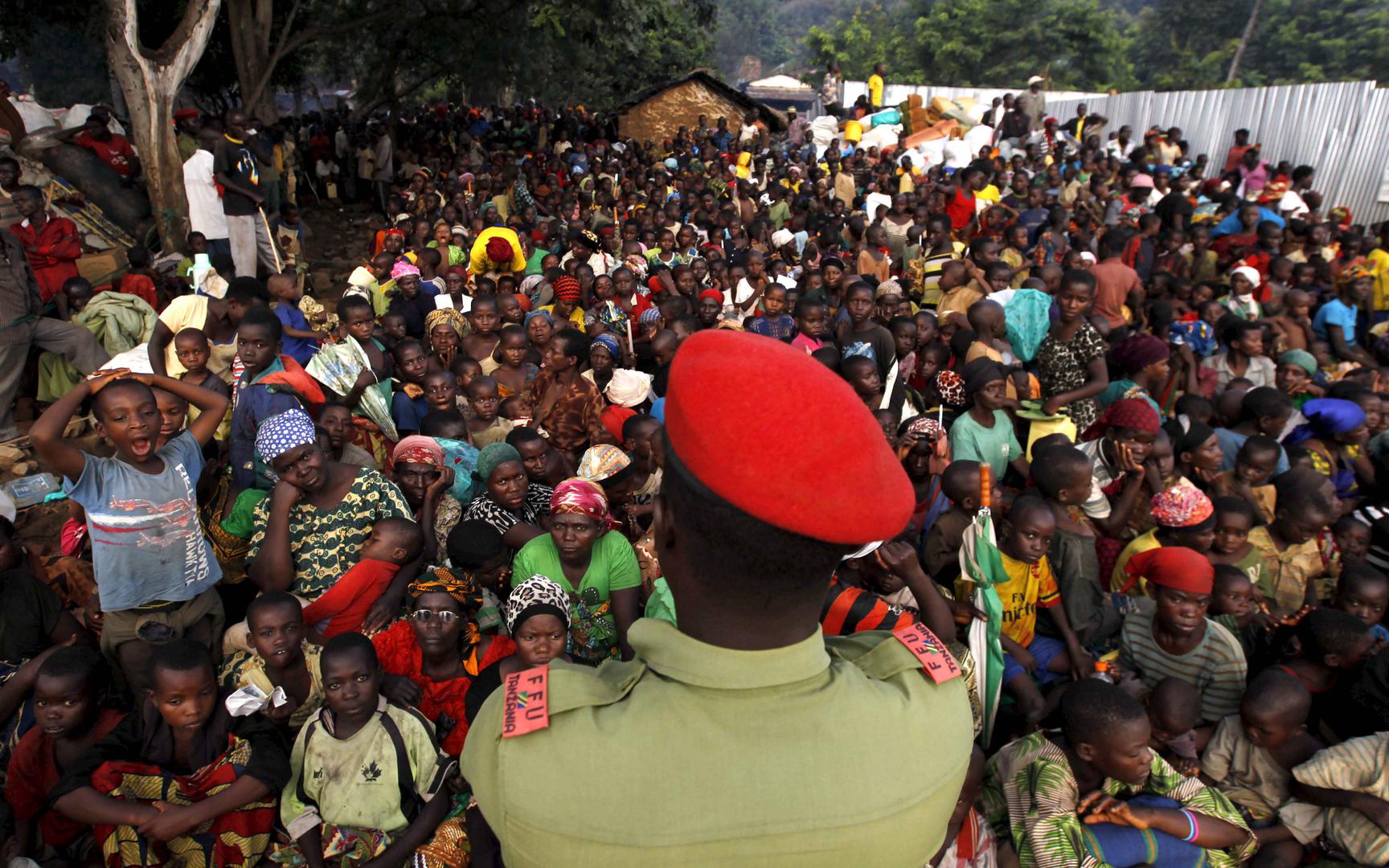 A Tanzanian policeman watches over as Burundian refugees gather on the shores of Lake Tanganyika in Kagunga village in Kigoma region in western Tanzania, where they wait for transport to Kigoma township, May 17, 2015.