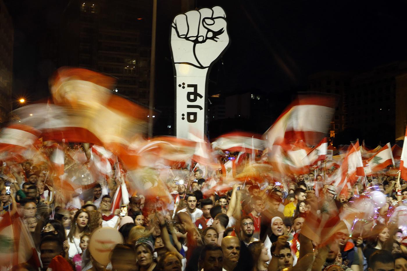 Anti-government protesters wave Lebanese flags during ongoing anti-government protests, in Beirut, Lebanon, November 10, 2019. The Arabic on the fist reads "Revolution."