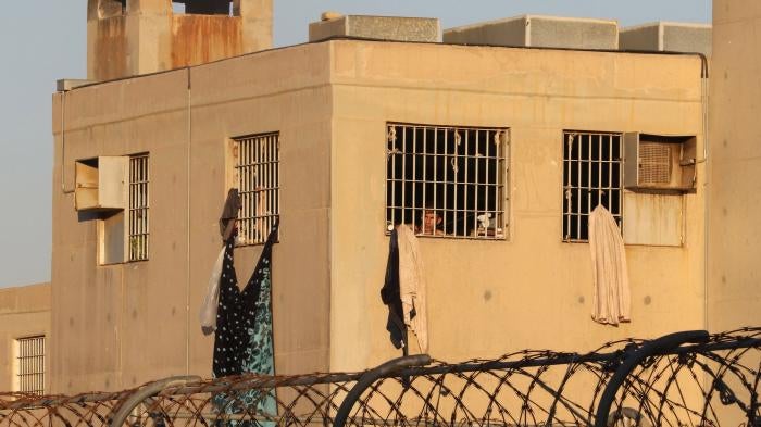 A man looks out from behind the bars of a prison building