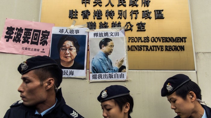 Police walk past missing person notices for Swedish publisher Gui Minhai (L) and Hong Kong publisher Yau Wentian, posted on the sign of China's Liaison Office in Hong Kong, January 3, 2016.