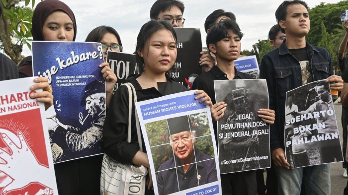 Demonstrators hold placards depicting the late Indonesian President Suharto during a rally against a government proposal to name him a “national hero”