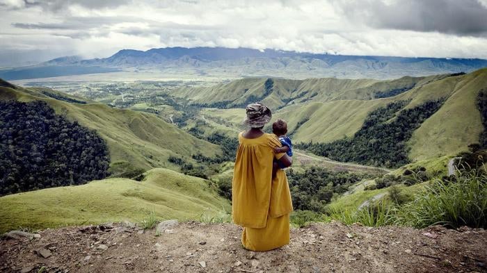 A woman holding a child looks down the valley from Kassam Pass.