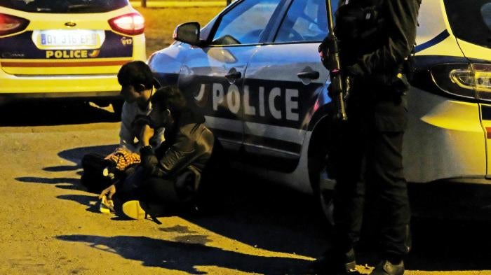 French police detain two migrants, one a 14-year-old boy, before dispersing a late-night food distribution in Calais on June 29, 2017. 