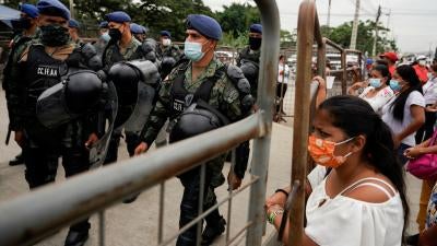 Soldiers walk carrying riot gear, while civilians look in behind barricades