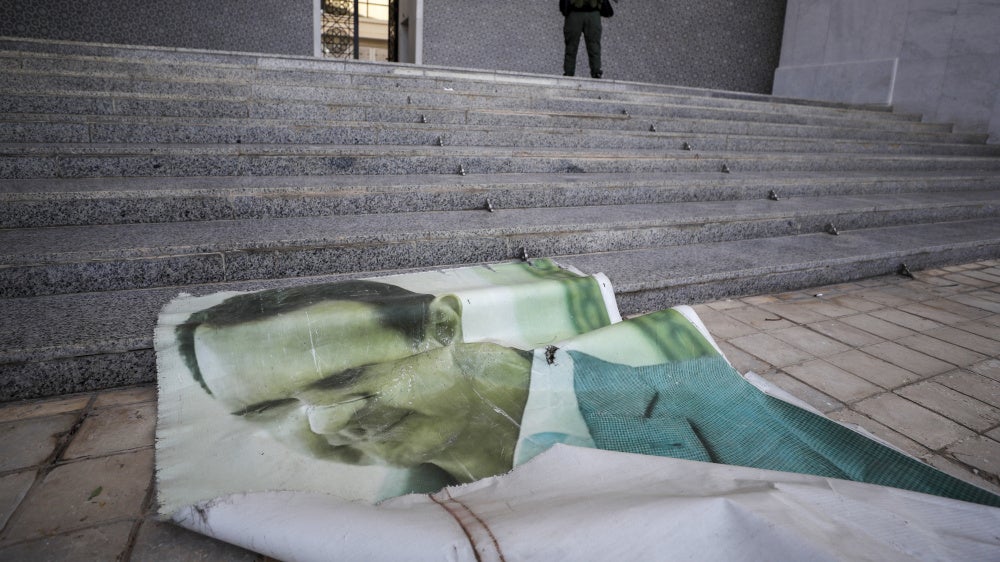 A picture of former Syrian President Bashar Assad lies on the ground as a Syrian opposition fighter stands nearby, inside the Presidential Palace in Damascus, December 8, 2024.
