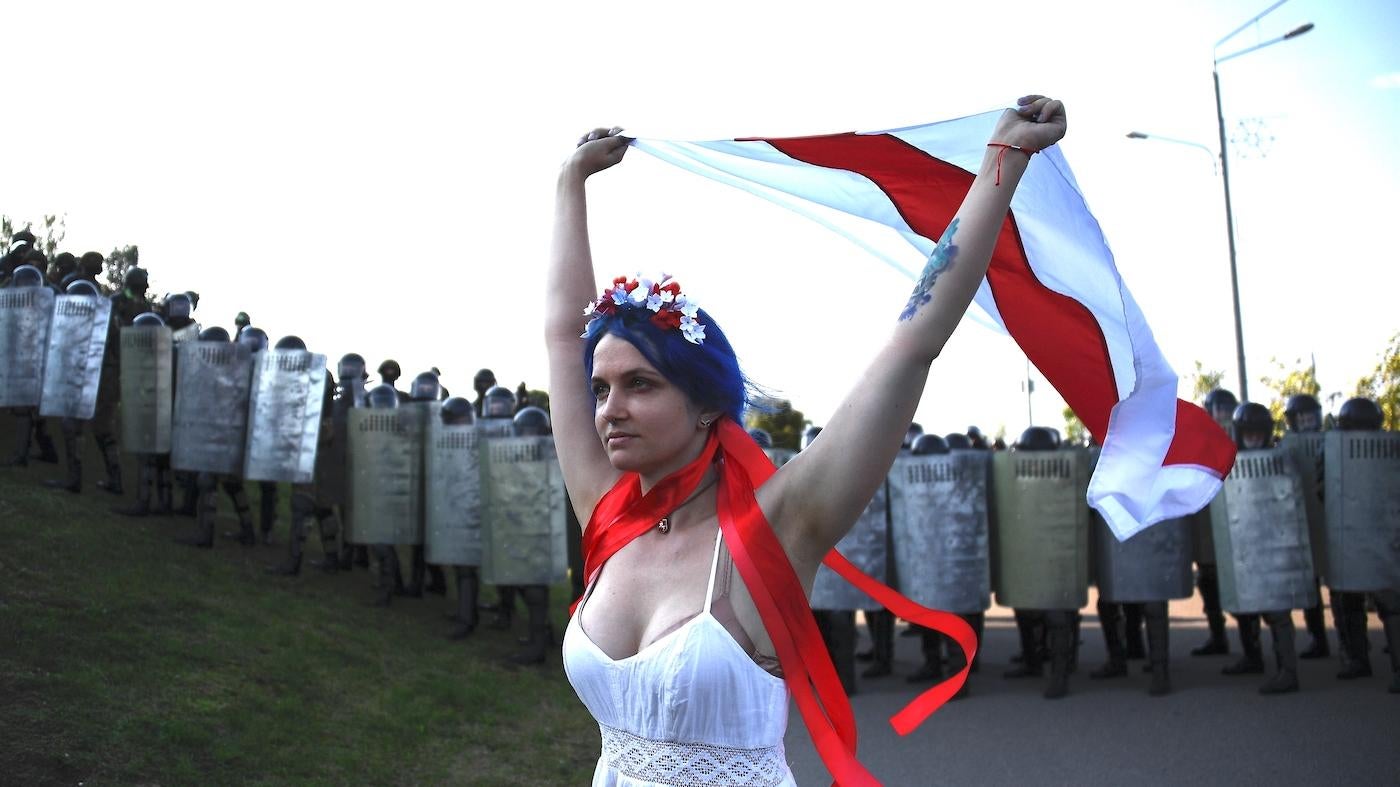 A woman carries a white-red-white flag as law enforcement officers block the street during an opposition rally against presidential election results in Minsk, Belarus.