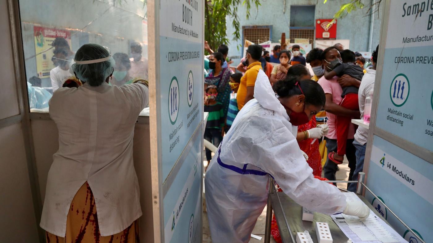 People wait to get tested for Covid-19 in Hyderabad, India. A crowd stands before two health care workers. 