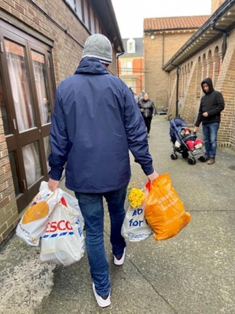 A man in a coat walks down a street carrying grocery bags