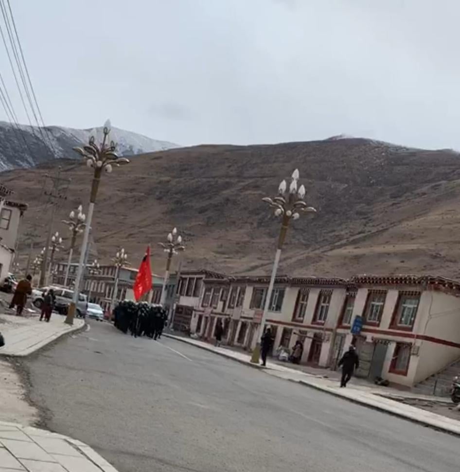 Screenshot of a video showing dozens of police and commandos parading through the town of Dza Wonpo, carrying a large red flag and shouting battle-cries.