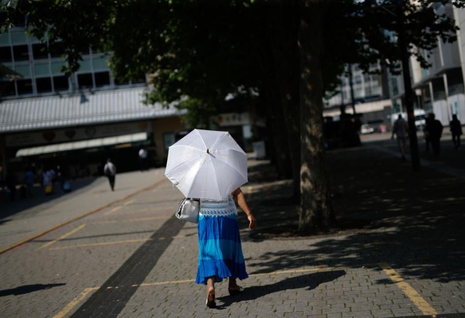 A woman walks under a parasol to shelter from the sun in Birmingham, U.K., on Tuesday, July 20, 2021. The U.K.'s Met Office has issued its first-ever Extreme Heat weather warning, stating that continuing high temperatures will lead to public health impacts.
