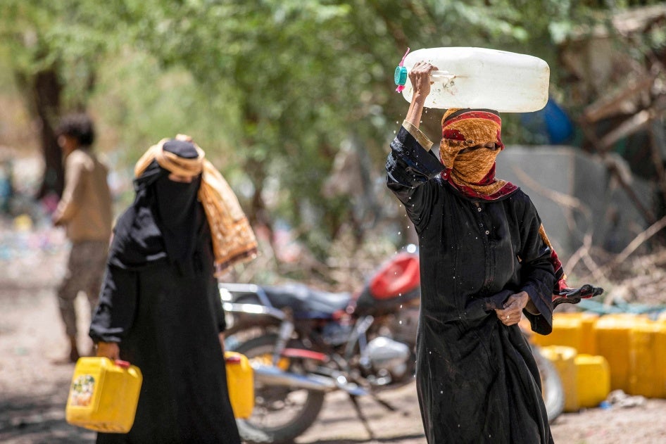 Women walk with canisters filled with water from a tanker truck on the outskirts of Taizz.