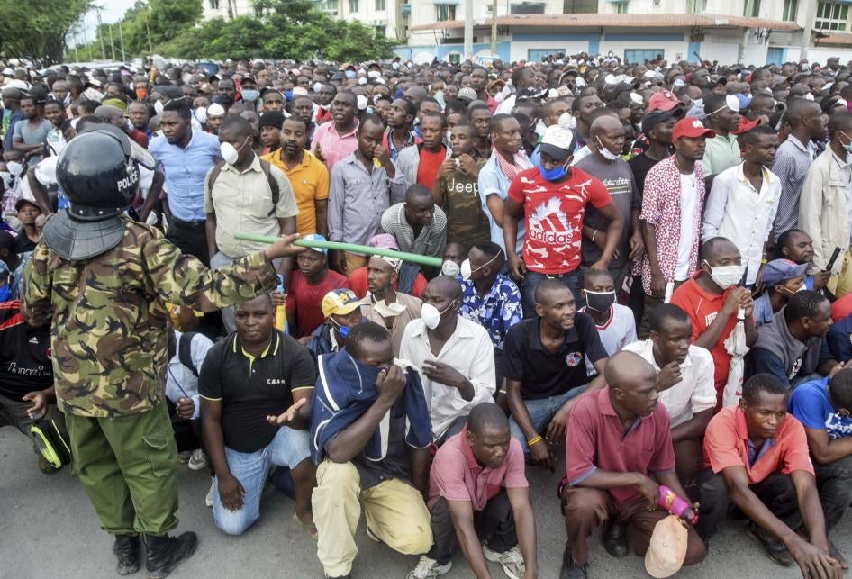 Un policier kenyan brandit un bâton devant une foule de personnes qui attendent afin de pouvoir monter à bord d’un ferry au port de Mombasa, le 27 mars 2020.