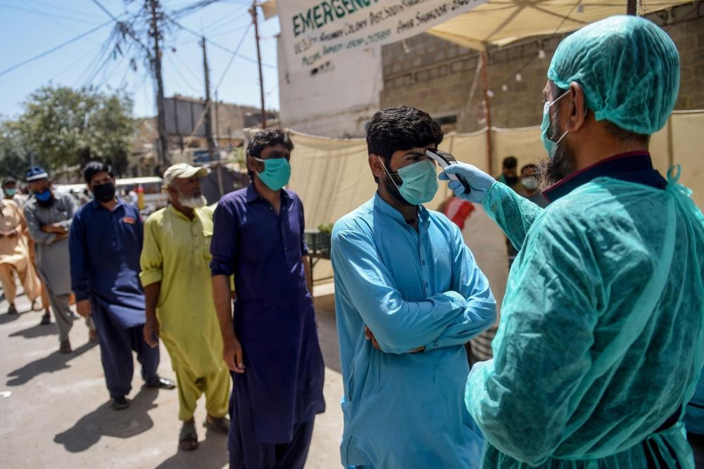 Men are lined up in face masks to receive a temperature check