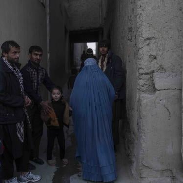 A woman wearing a burqa walks by a group of men 