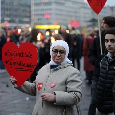 Syrian refugees hold a protest sign that reads "Syria Not Safe"