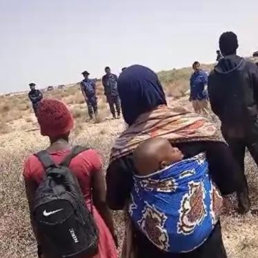 A group of Black migrants and asylum seekers of multiple African nationalities, including a woman and her baby, stranded in the desert for days after expulsion from Tunisia, stand in the buffer zone at the Tunisia-Libya border facing an Al Jazeera news crew and Libyan soldiers, July 11, 2023.