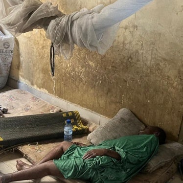 Aisha stands by her mother, lying on a worn-out and dirty mattress.