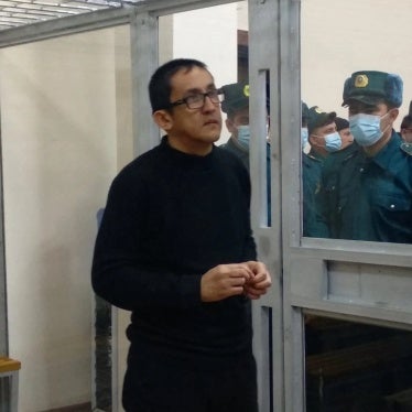 A man stands inside a glass defendants cage in a courtroom