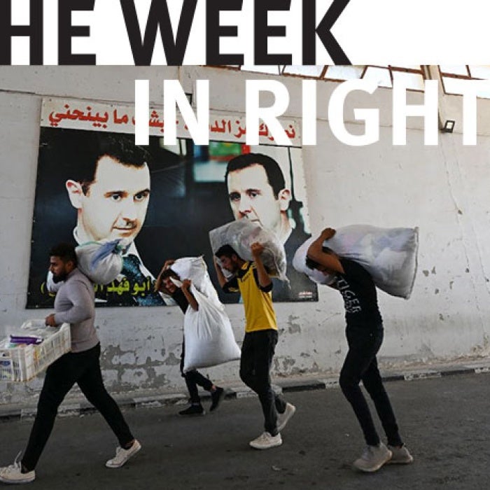 Four figures carry their belongings on street. 