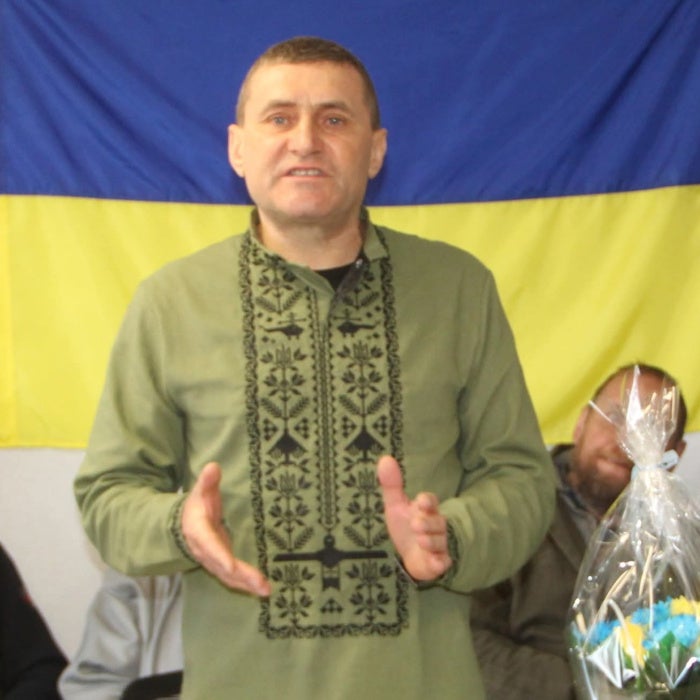 A man speaks in front of a Ukrainian flag
